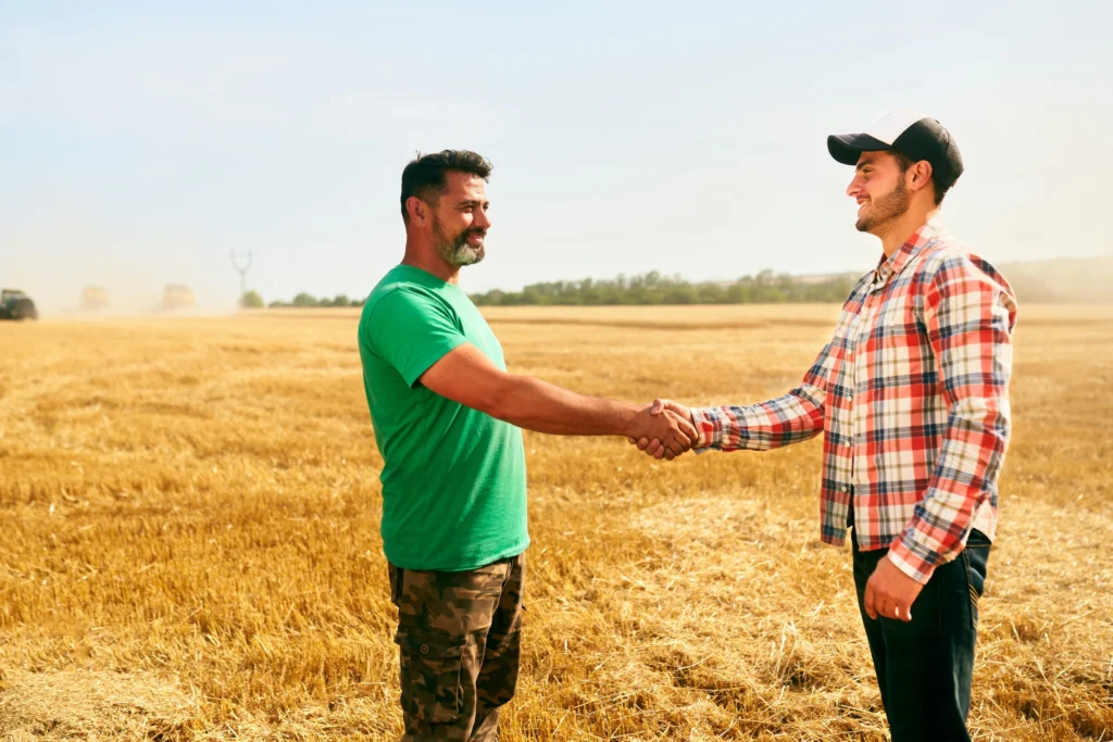 Dans un champ de céréales, deux personnes, dont l'agriculteur se serrent la main