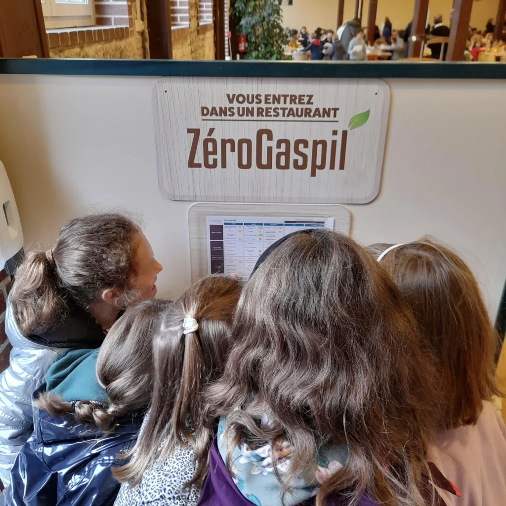 De jeunes enfants devant le panneau Zéro Gaspil' affiché à l'extérieur de la cantine
