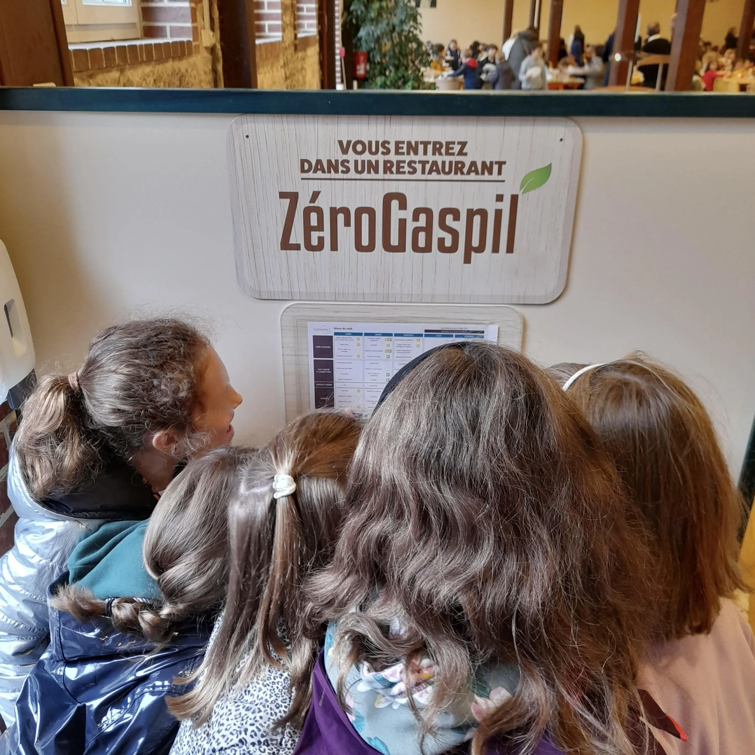 De jeunes enfants devant le panneau Zéro Gaspil' affiché à l'extérieur de la cantine